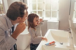 young girls brushes her teeth with her father in the morning