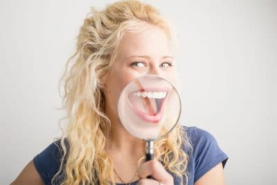 Attractive blonde woman with magnifying glass shows off her white smile