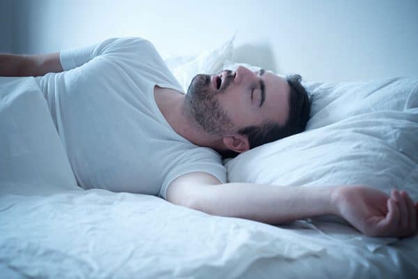 man sleeping in bed snores loudly with mouth wide open